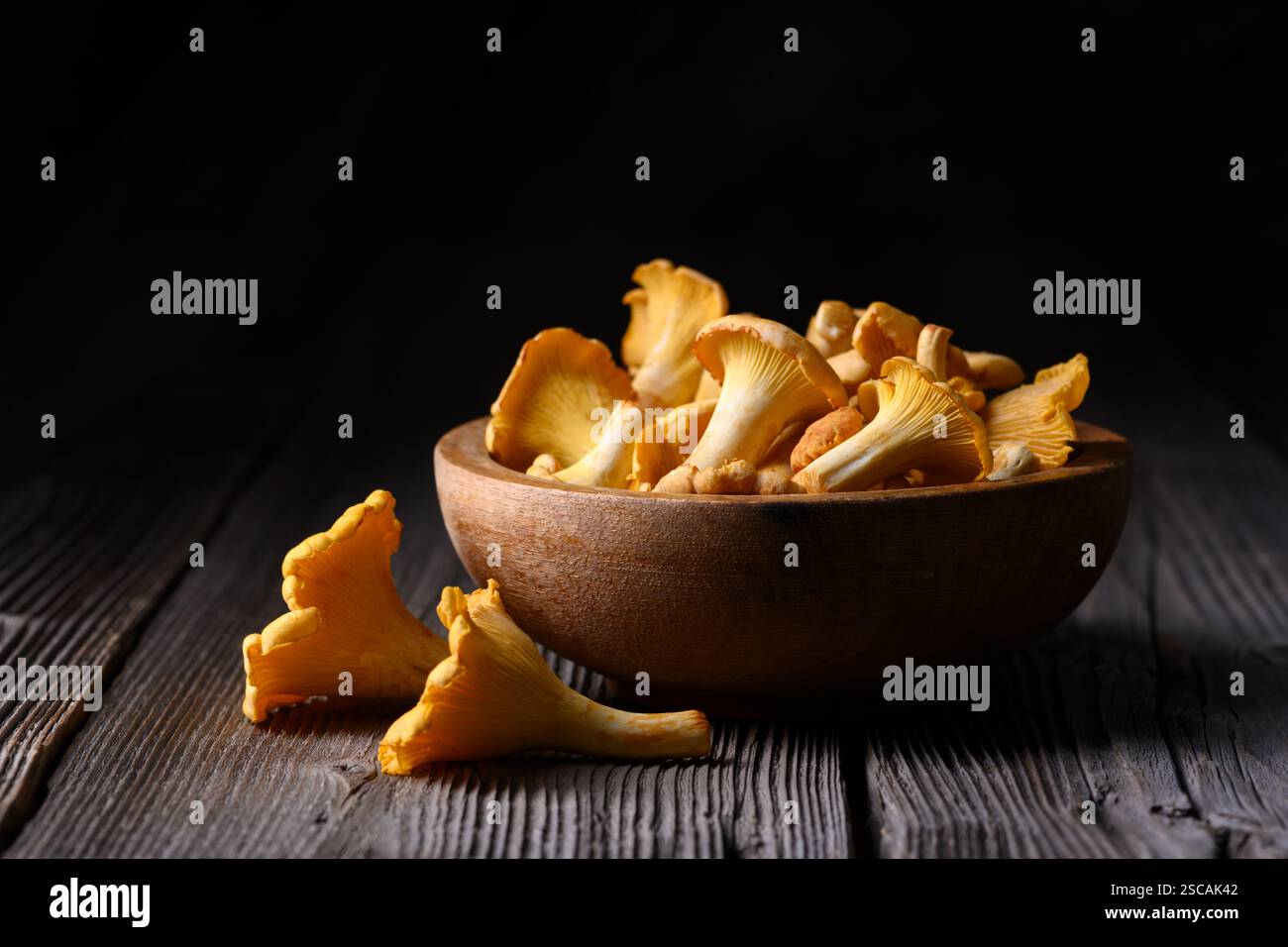Fresh Chanterelle mushrooms in a wooden bowl on rustic wooden table on dark background. Food photography Stock Photo