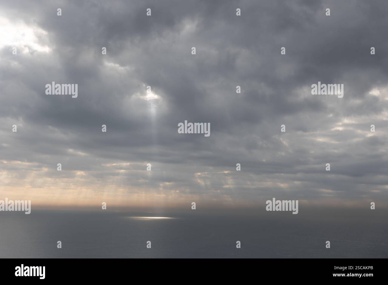 The sun rays breaking through gray clouds reflecting on the sea surface Stock Photo