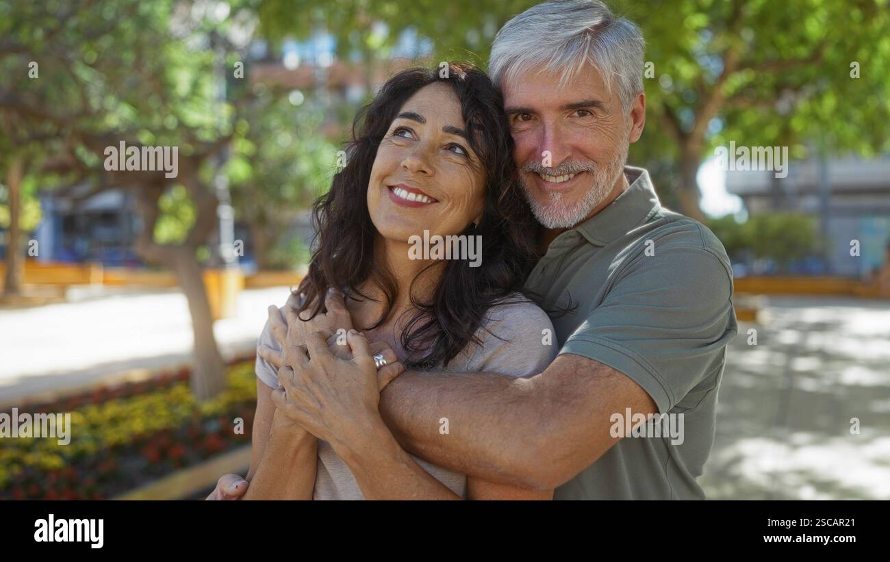 Middle-aged couple embracing warmly in a sunny urban park with trees ...