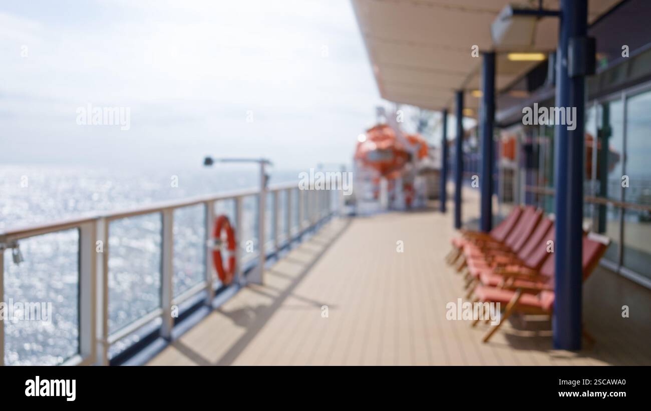 Luxury cruise deck with blurred view of deck chairs, railing, and ocean in bright sunlight, highlighting defocused coastal scenery and bokeh of shimme Stock Photo