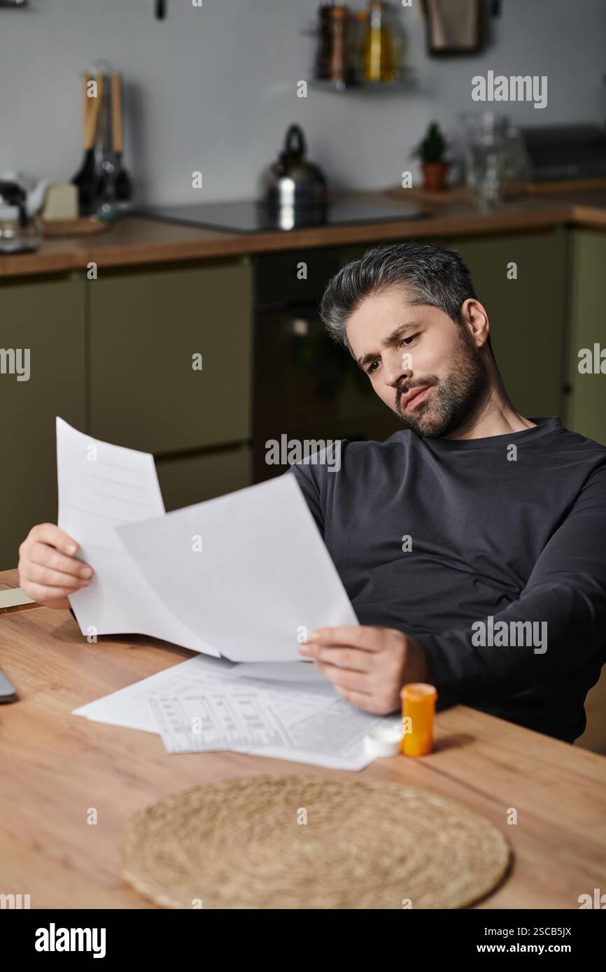 A handsome man studies printed papers at a well arranged kitchen table. Stock Photo