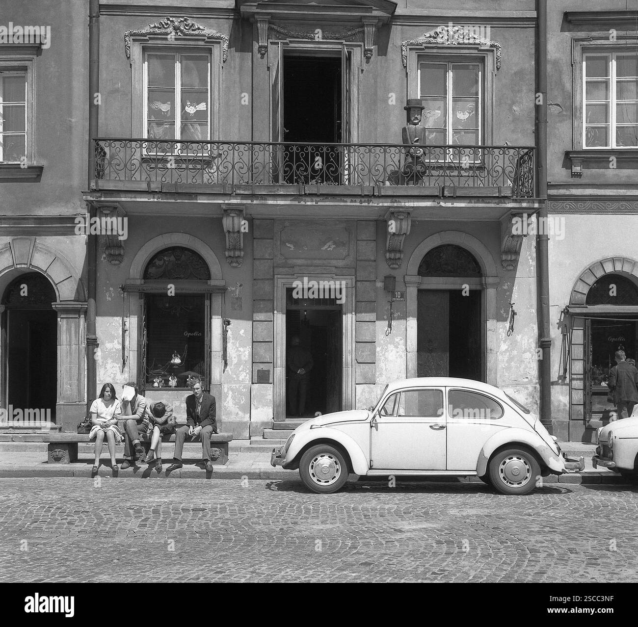 Youths on a bench, a house with balcony and a Volkswagen-Beetle in ...