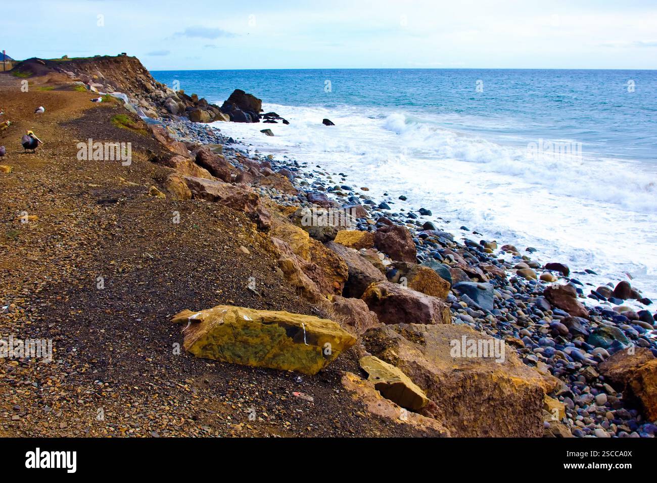 Rocky shoreline with a beach in the distance. The rocks are scattered ...