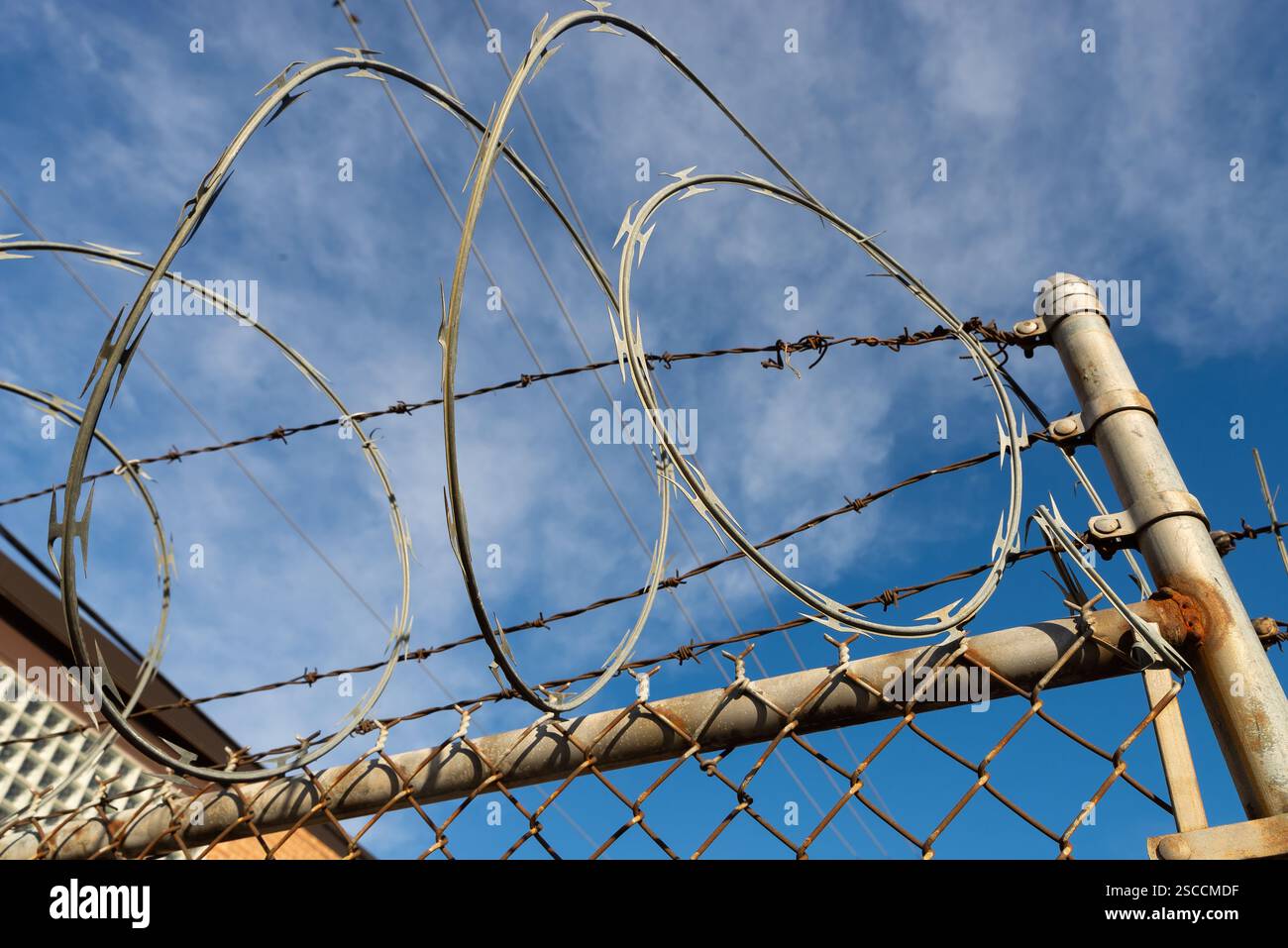 Razor wire on chain link fence with blue skies and clouds in the ...