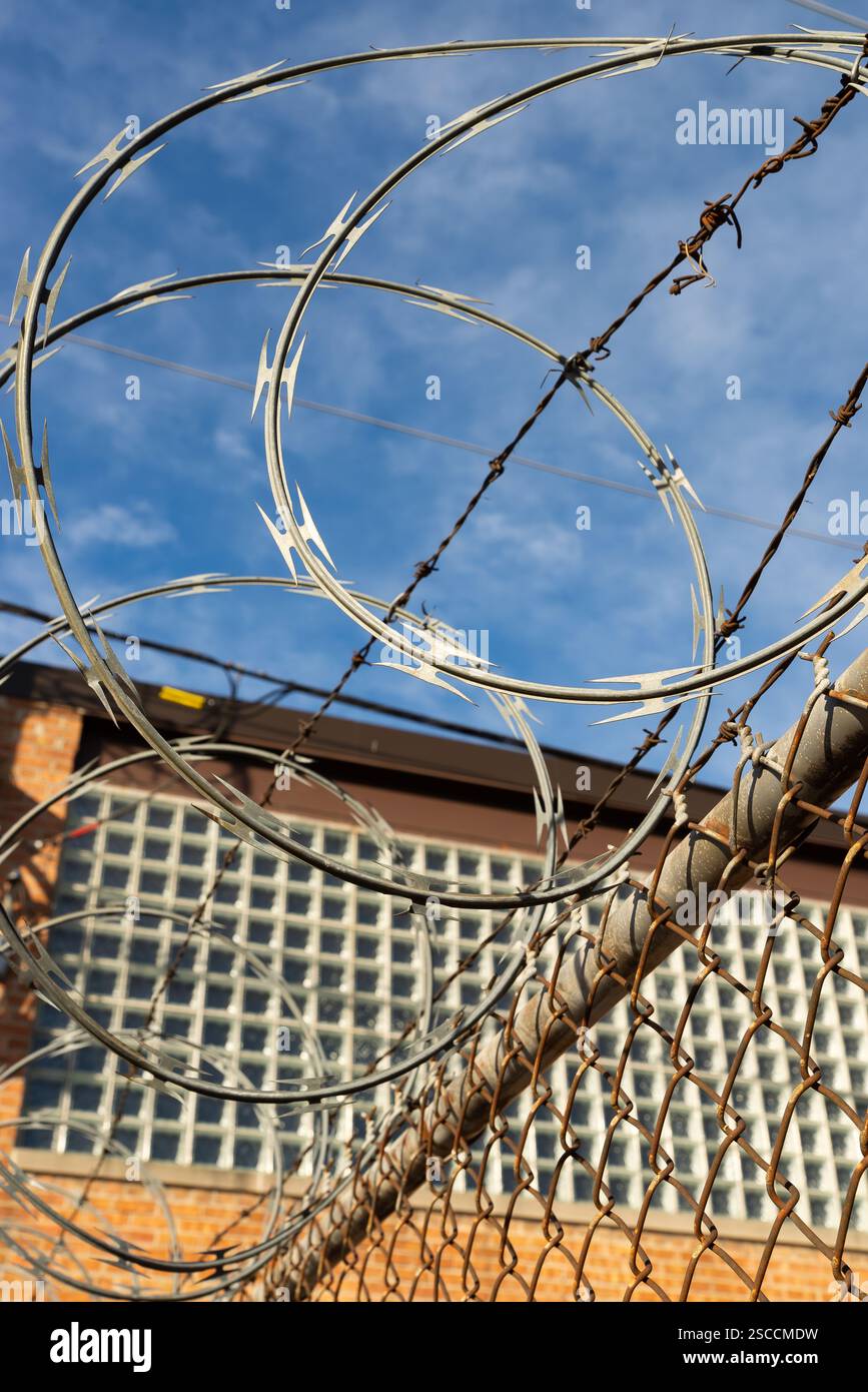 Razor wire on chain link fence with blue skies and clouds in the ...