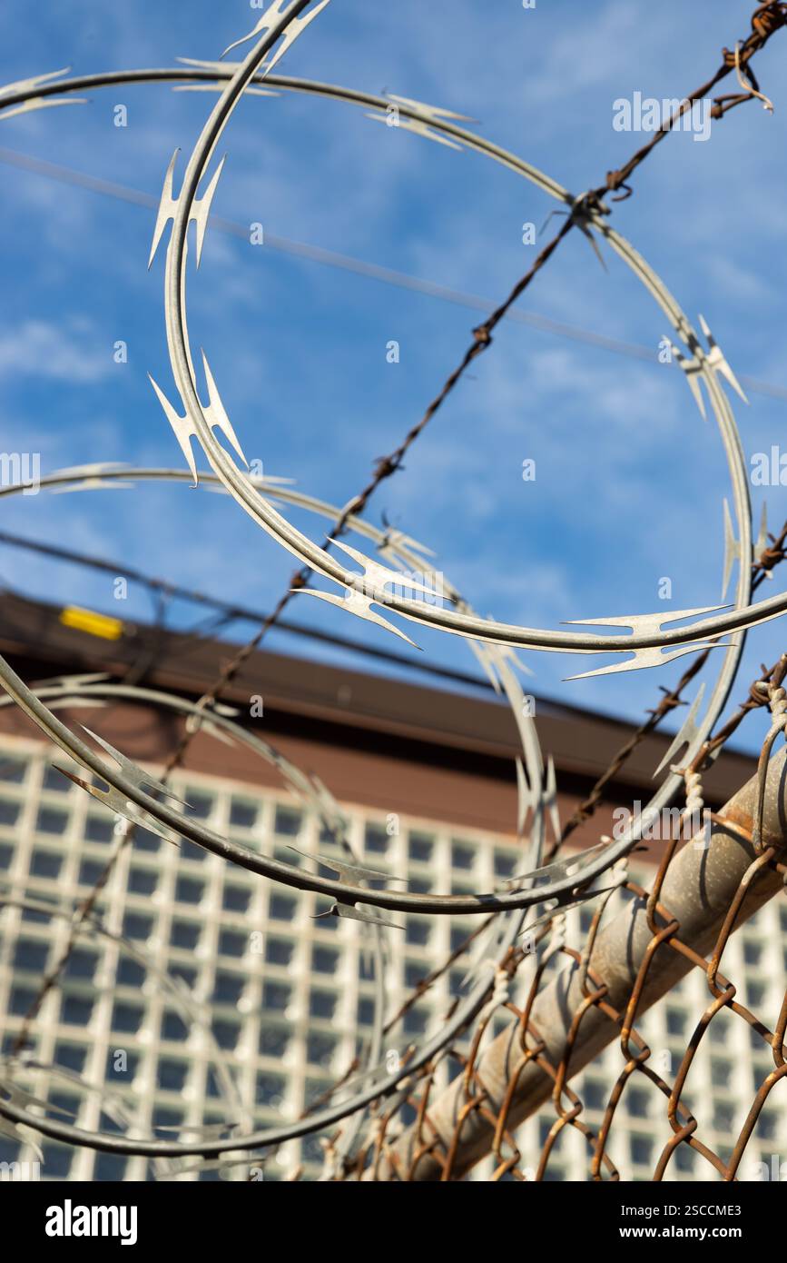 Razor wire on chain link fence with blue skies and clouds in the ...