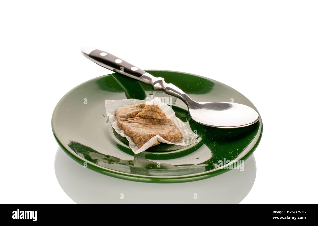 One used tea bag with a teaspoon on a ceramic saucer, close-up, isolated on a white background. Stock Photo