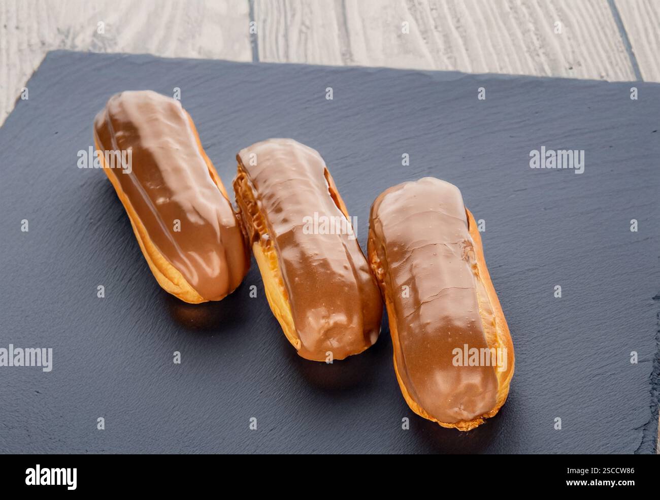 Three sweet eclairs on a slate stone, close-up. Stock Photo