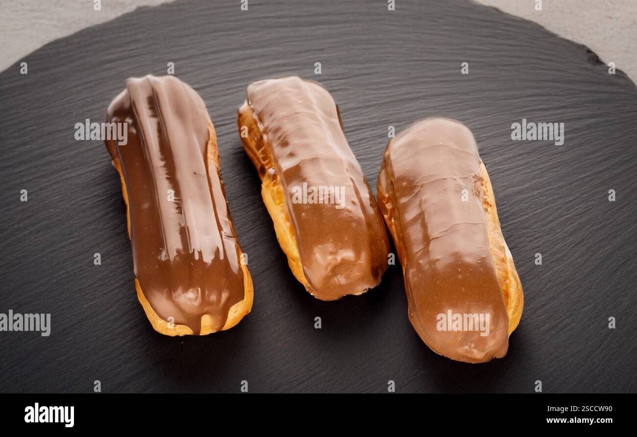 Three sweet eclairs on a slate stone, close-up. Stock Photo