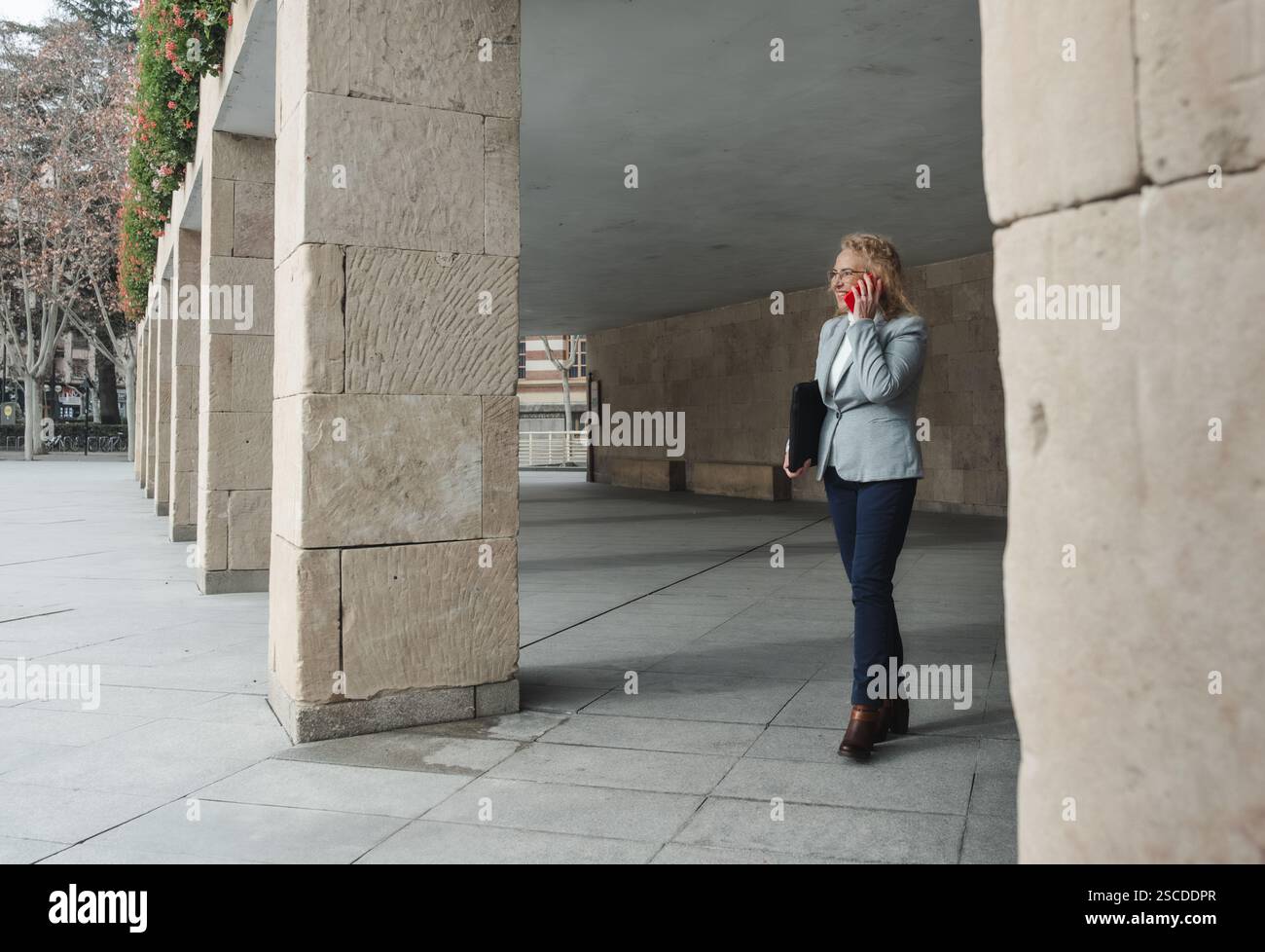 Businesswoman talking on phone while walking outdoors Stock Photo