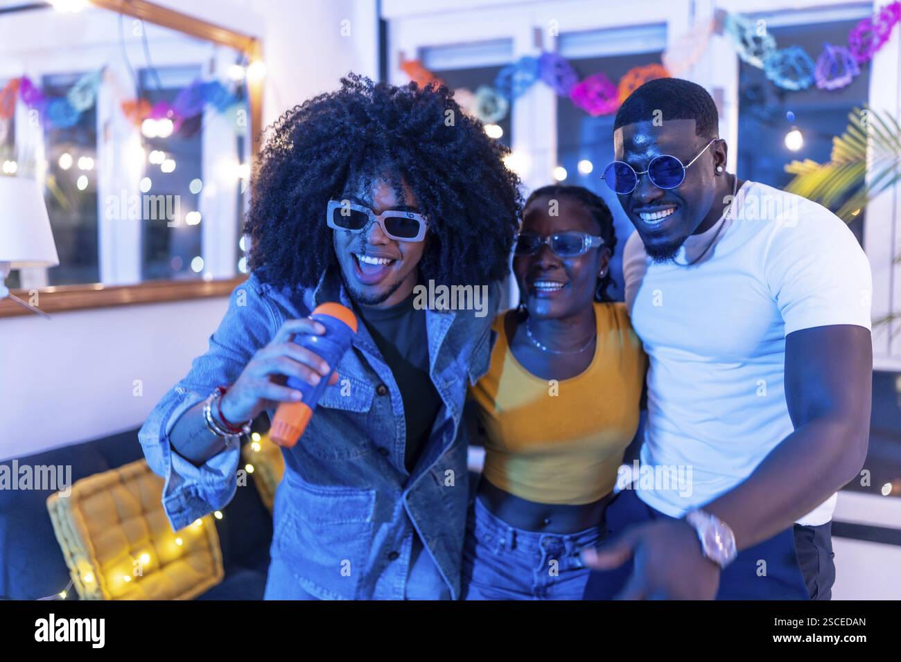 Multi-ethnic friends singing karaoke at home surrounded by blue neon ...