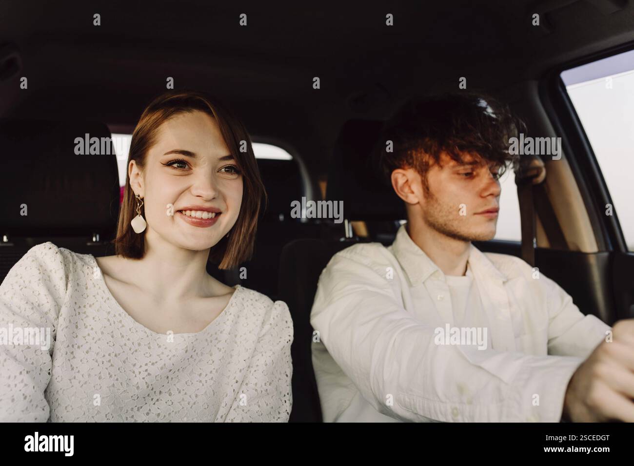 Woman smiling inside a car as the man focuses on driving Stock Photo