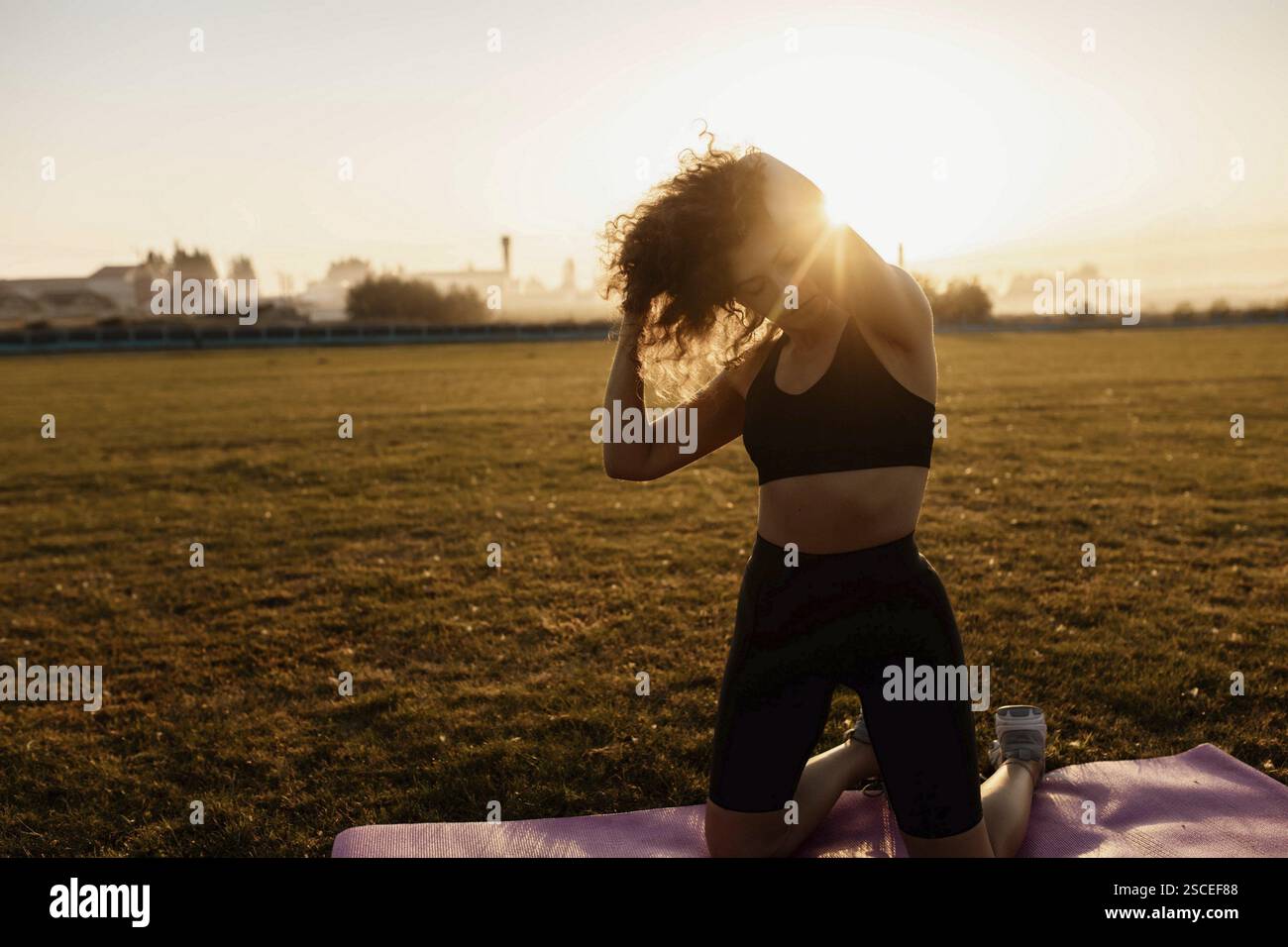 Woman adjusting hair while kneeling on a yoga mat in the sunlight Stock Photo