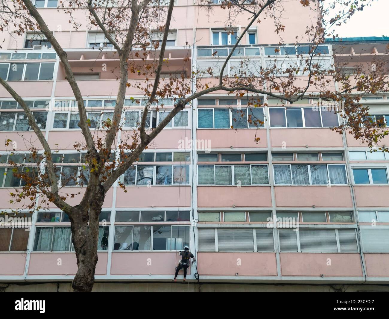 Construction worker painting exterior wall facade of apartment building hanging on industrial rope - Smartphone Captured Stock Image