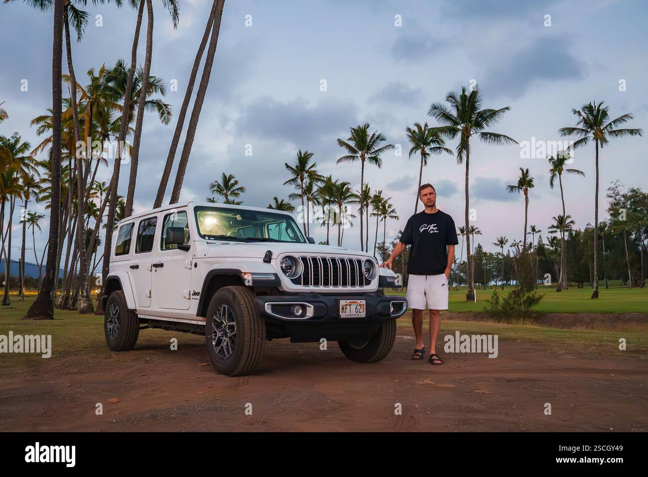 Man Standing by White Jeep Wrangler on Palm Lined Dirt Path in Hawaii Stock Photo