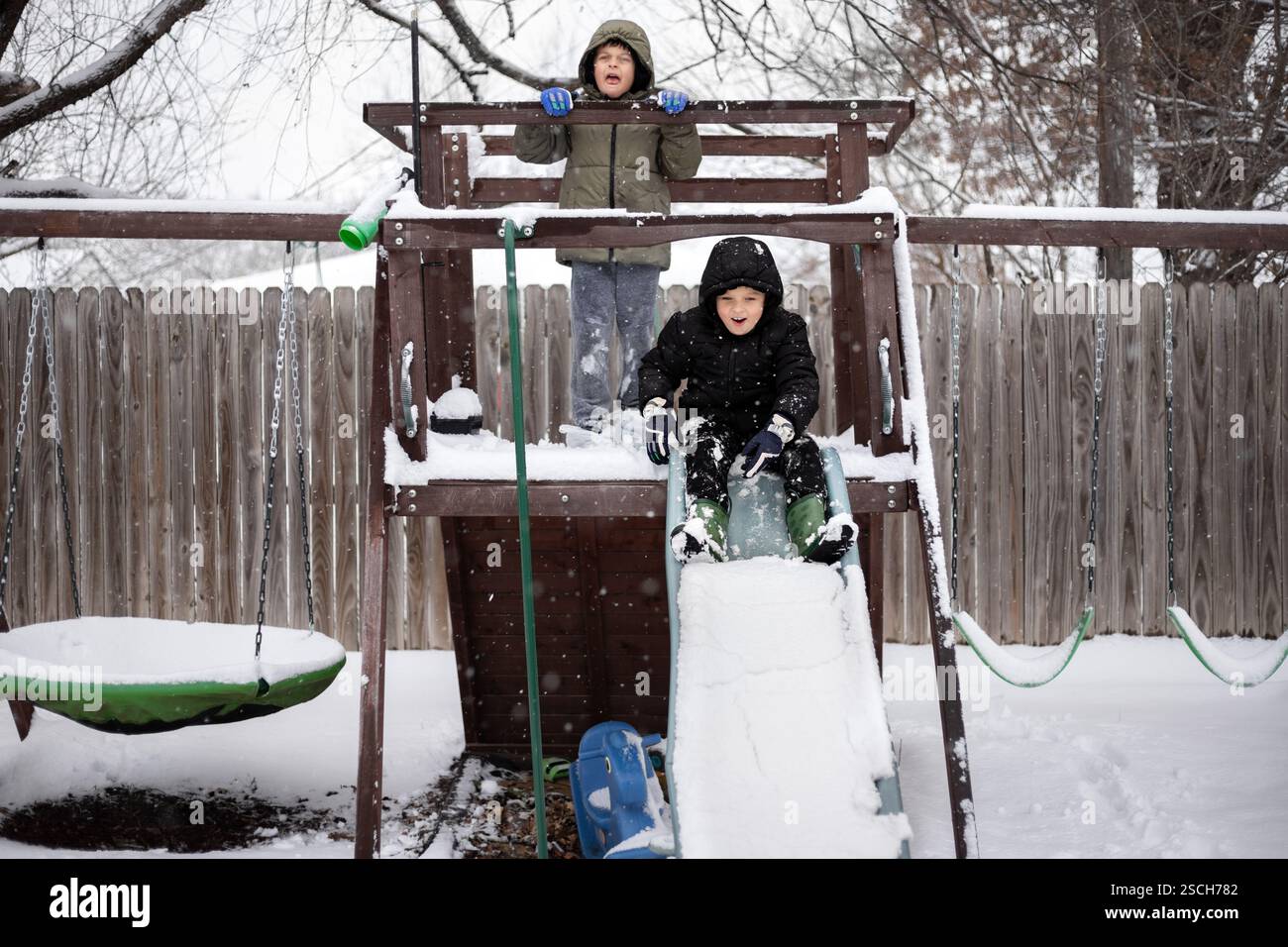 Two kids playing on snow covered slide and playset Stock Photo