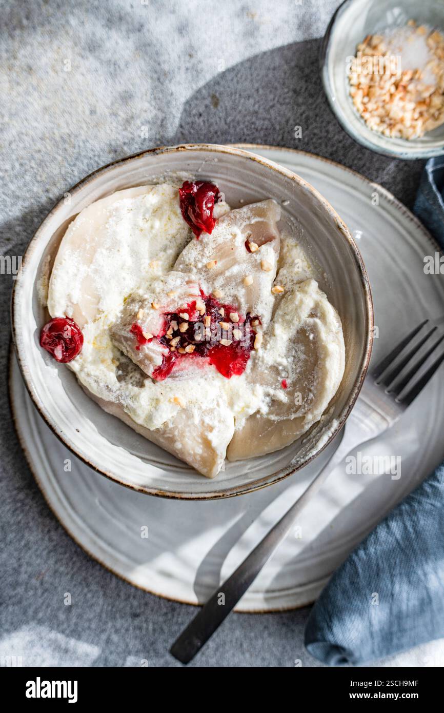 Traditional Ukrainian varenyky filled with cherries, served with creamy sour cream and sprinkled with chopped nuts. A delicious and authentic Eastern Stock Photo
