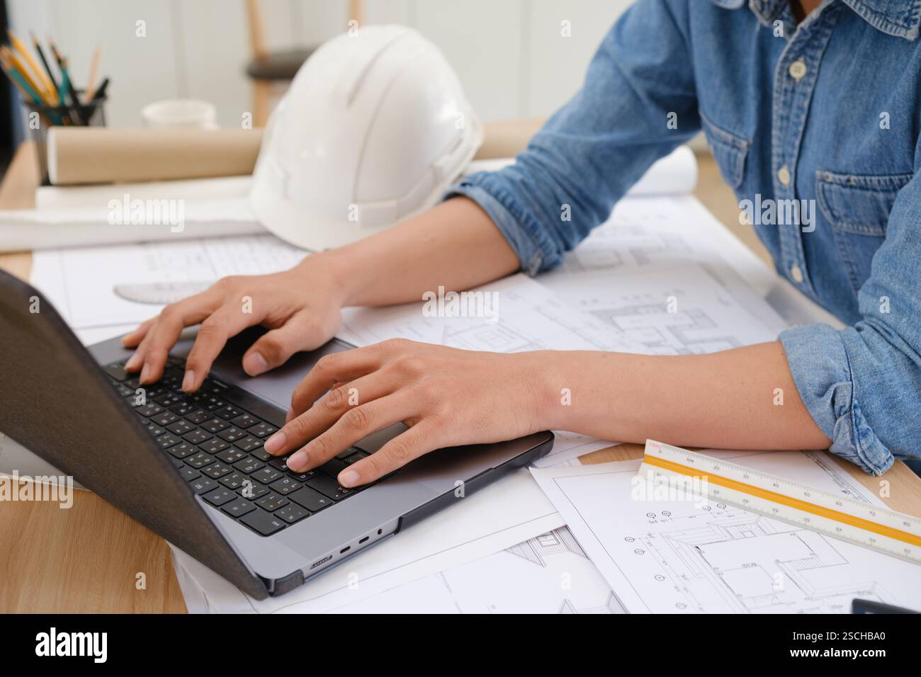 Architect and engineer working on blueprints using a laptop at a desk Stock Photo