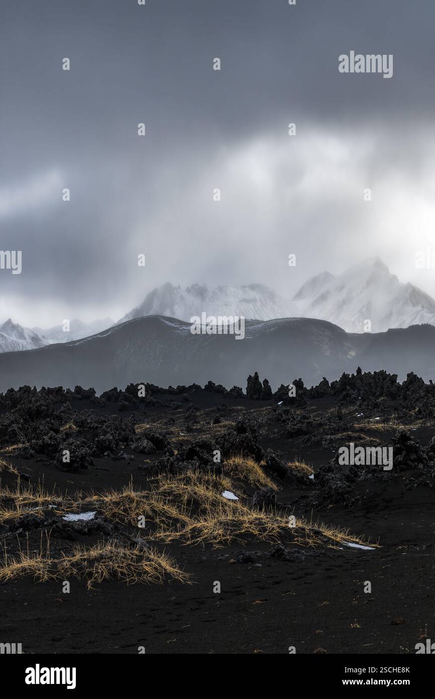 Captivating view of the Icelandic Highlands featuring rugged volcanic terrain, dark rocks, and snow-capped mountains under a dramatic cloudy sky. Stock Photo