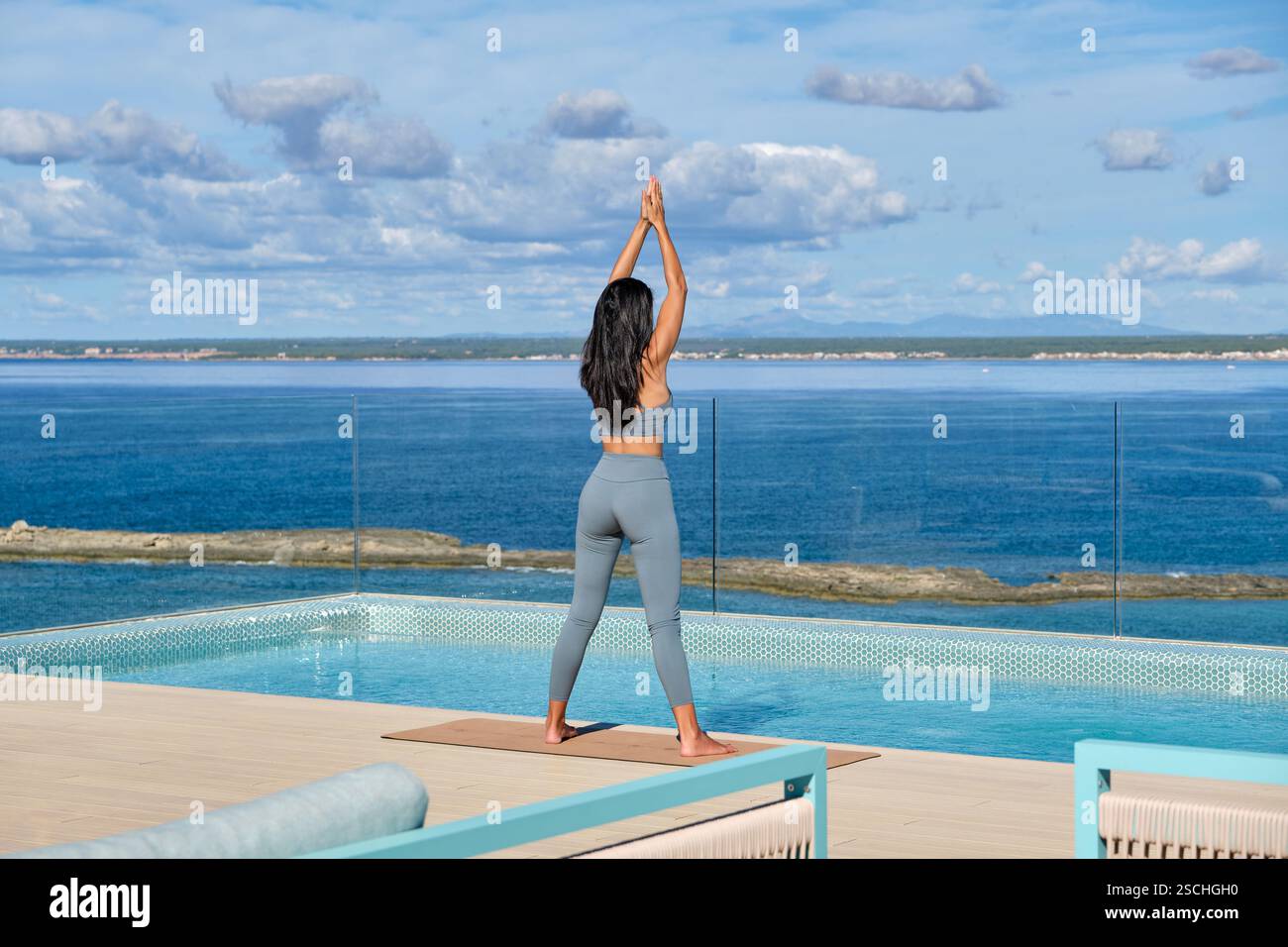 A woman in active wear performs yoga by an infinity pool overlooking ...