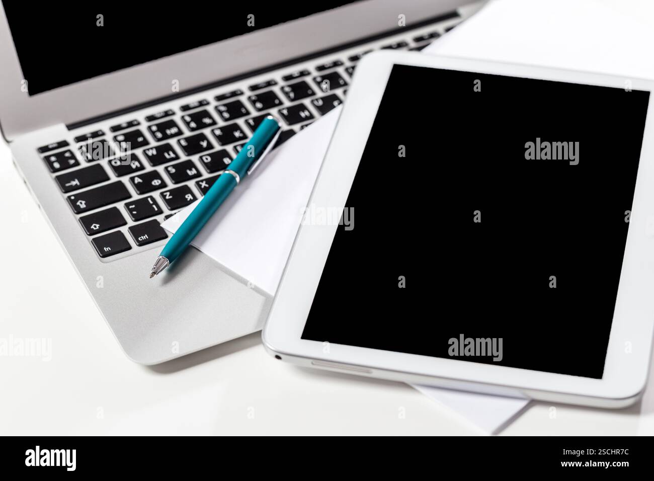 Workspace setup featuring laptop, tablet, pen, and blank sheets for productivity and creativity Stock Photo