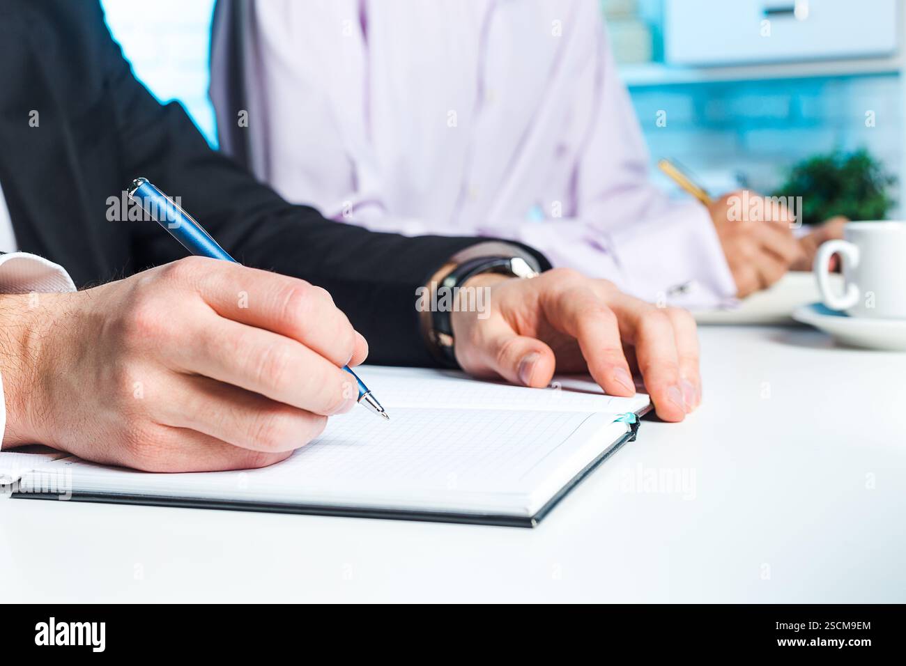 Professionals engaged in a meeting, taking notes at a modern workspace ...