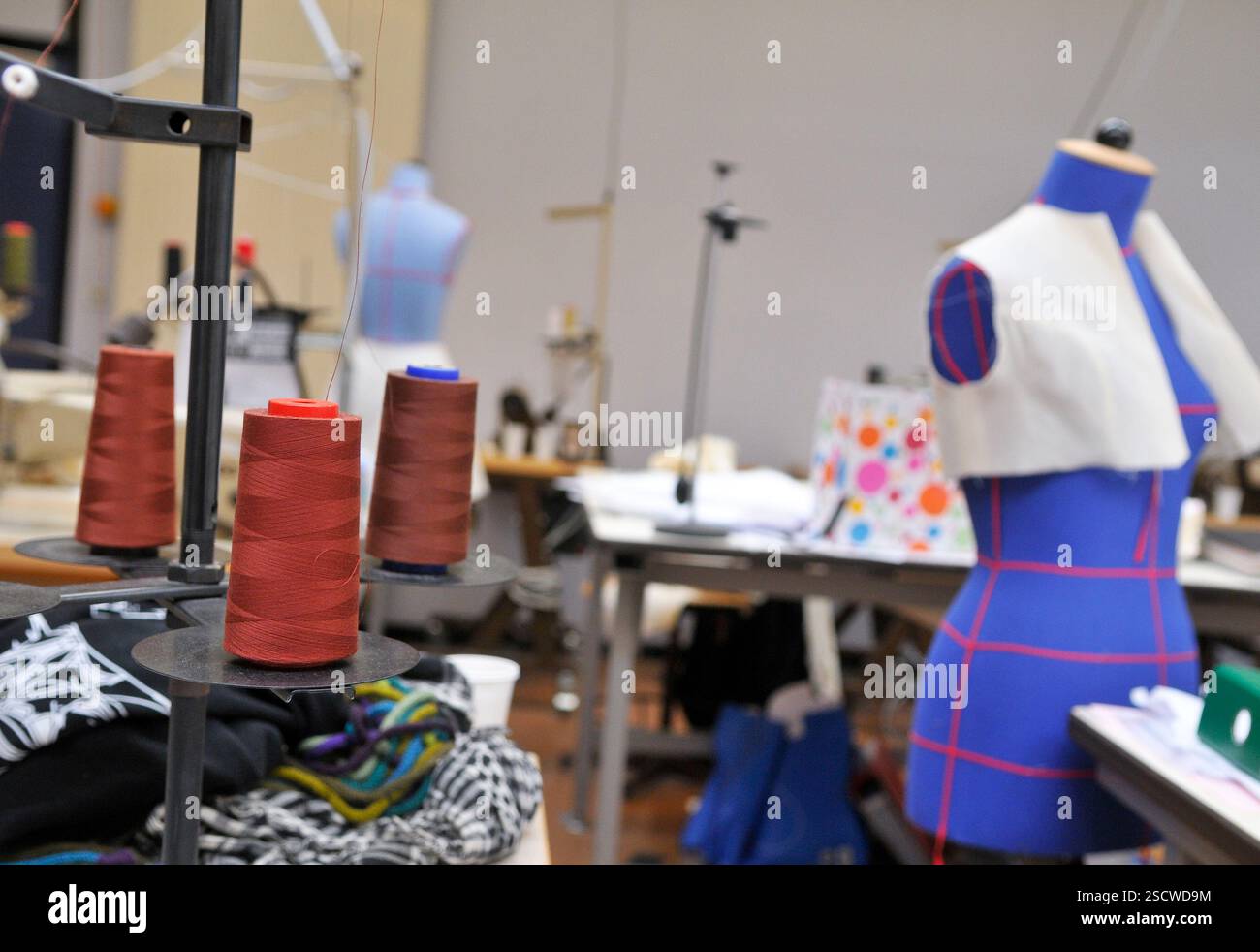 General view of a sewing workshop. Three spools of thread and a sewing mannequin in the foreground. Stock Photo