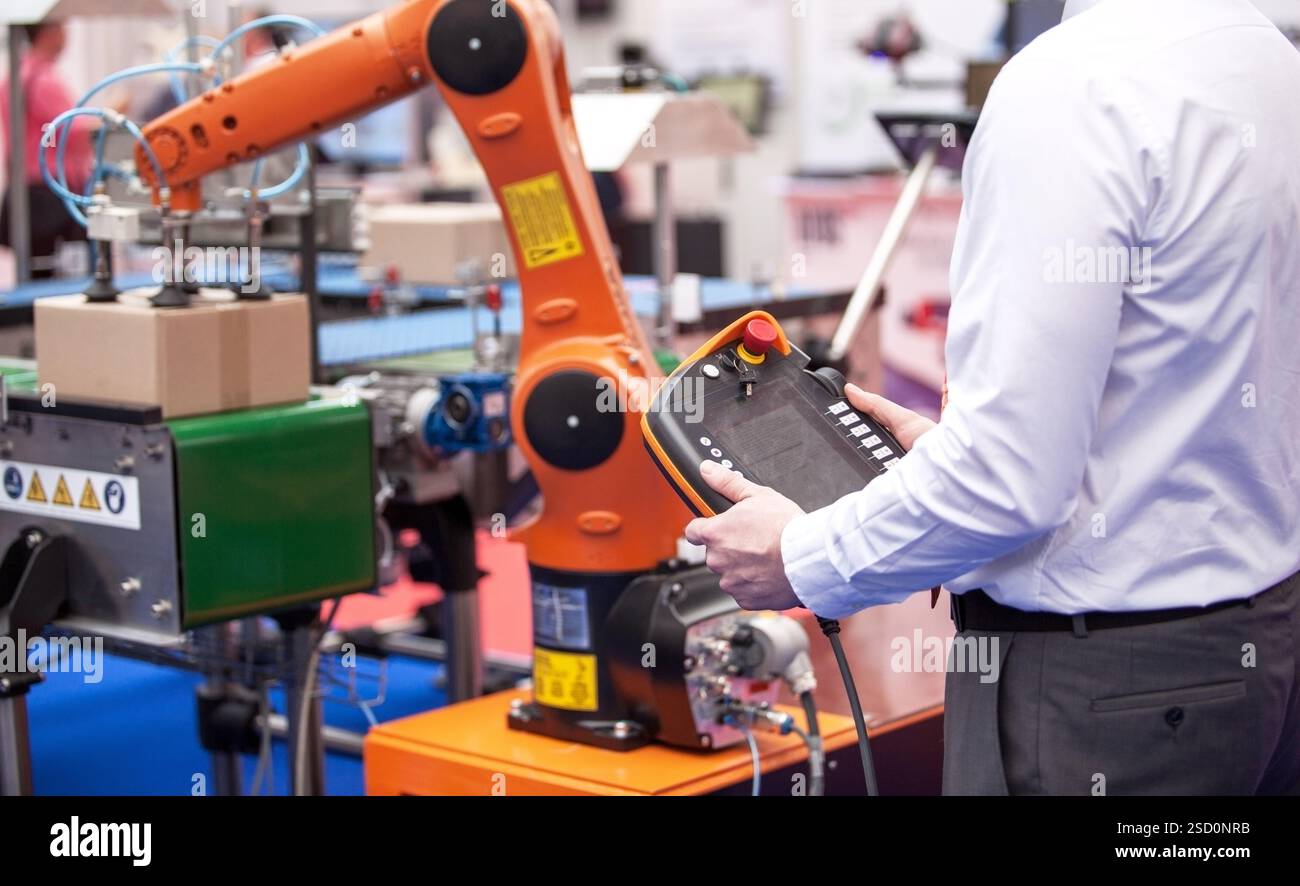 Engineer utilizing a control panel to operate a robotic arm in a automated industrial packing system Stock Photo