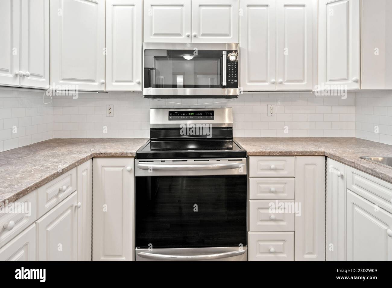 Kitchen with a white stove and microwave. The stove is black and silver. The kitchen is clean and well-organized Stock Photo