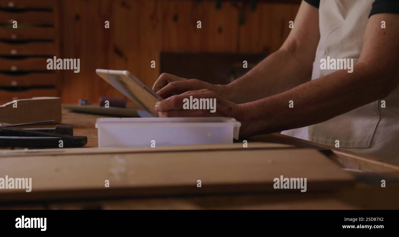 Carpenter using tablet in workshop, planning woodworking project with tools nearby Stock Photo