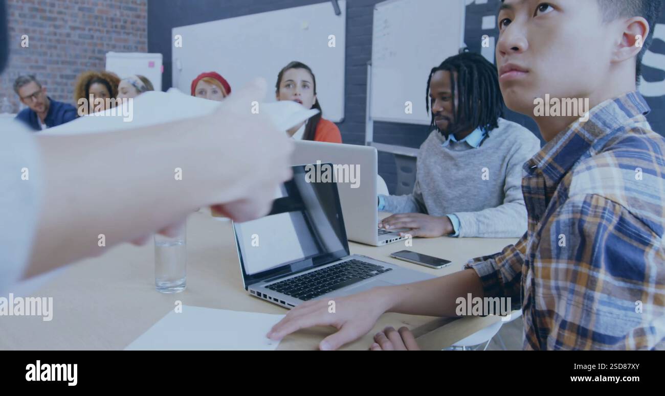 In office, diverse team collaborating on project with laptops and documents on table Stock Photo