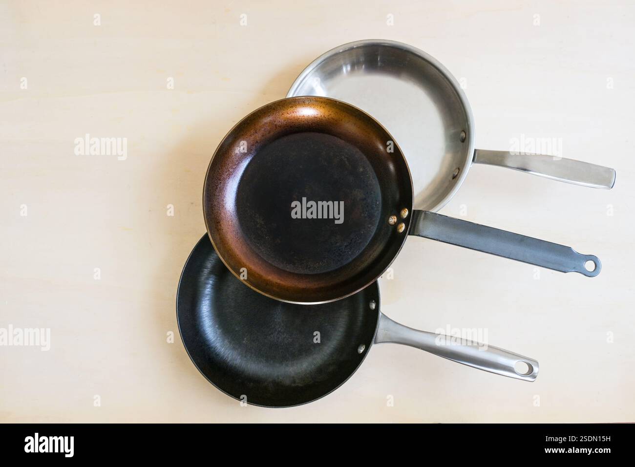 Three frying pans from natural material for healthy cooking made of carbon steel, stainless steel and cast iron without unhealthy non-stick coating, c Stock Photo