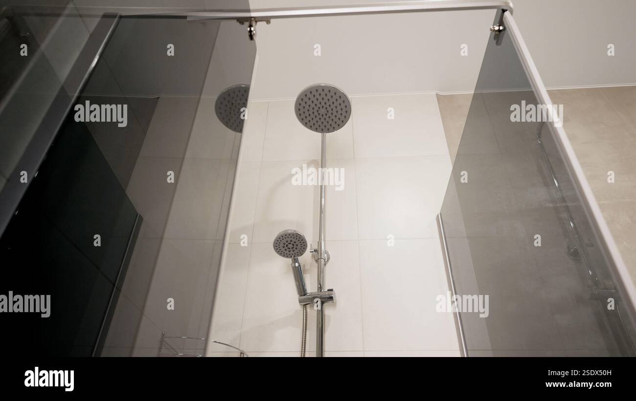 Chrome shower head with handheld sprayer highlighting sleek design, modern bathroom interior featuring minimalist white tiles and clean architectural Stock Photo