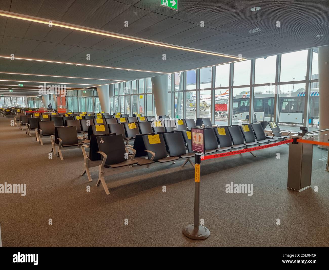 Empty chairs near a gate in airport terminal during COVID-19 pandemic with signs telling that alternate seats should be unoccupied to keep distance - Smartphone Captured Stock Image