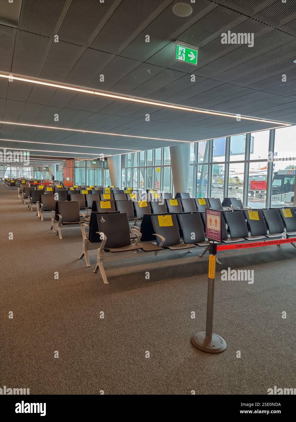 Empty chairs in airport terminal during COVID-19 pandemic with signs telling that alternate seats should be unoccupied to keep distance - Smartphone Captured Stock Image