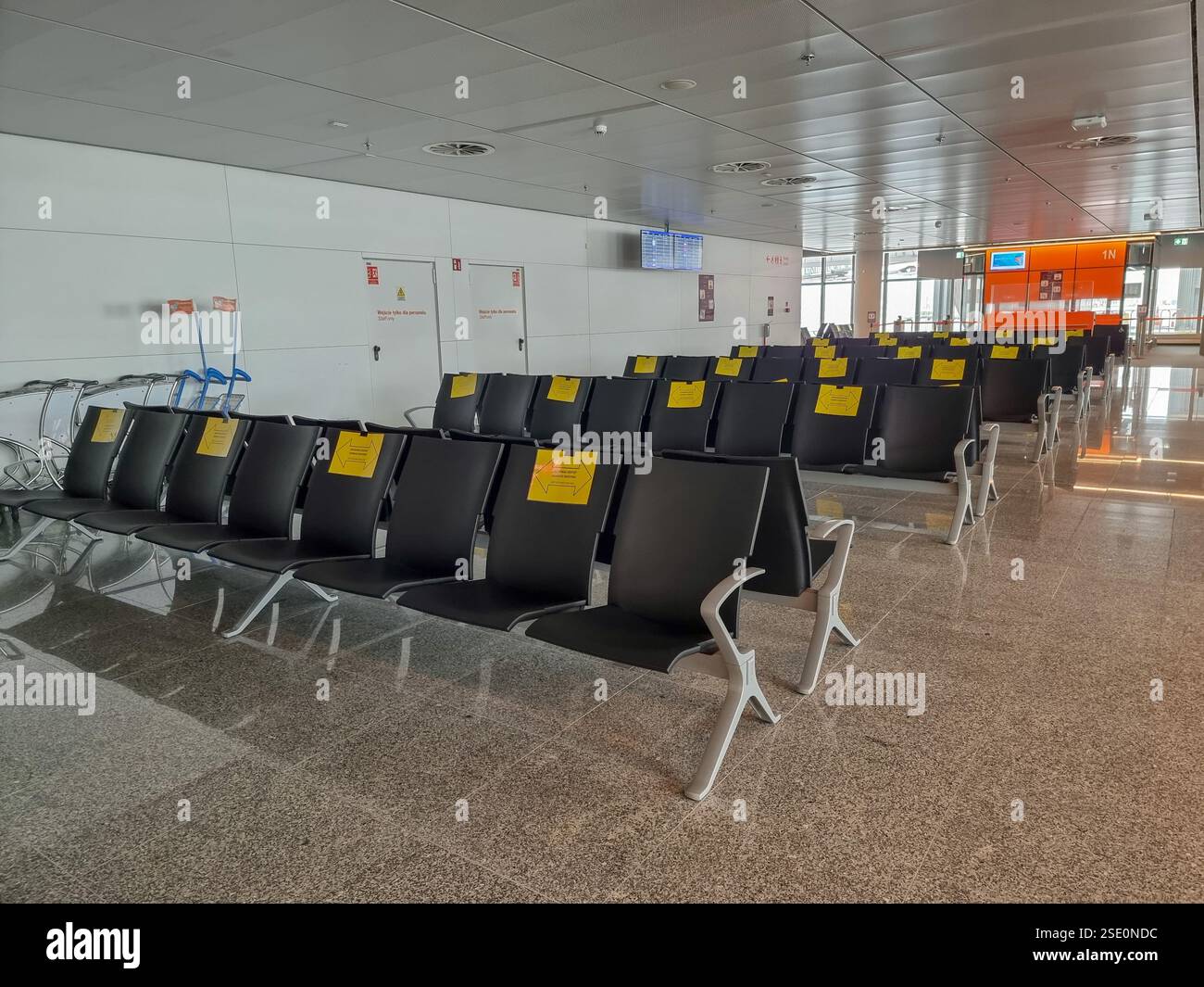 Empty chairs in airport terminal during COVID-19 pandemic with signs telling that alternate seats should be unoccupied to keep distance - Smartphone Captured Stock Image