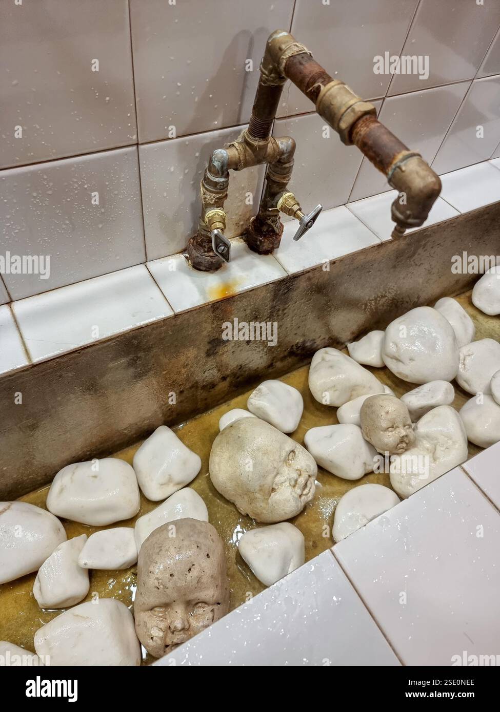Wash basin / sink with stones and child's heads from stone; bronze tap - Smartphone Captured Stock Image