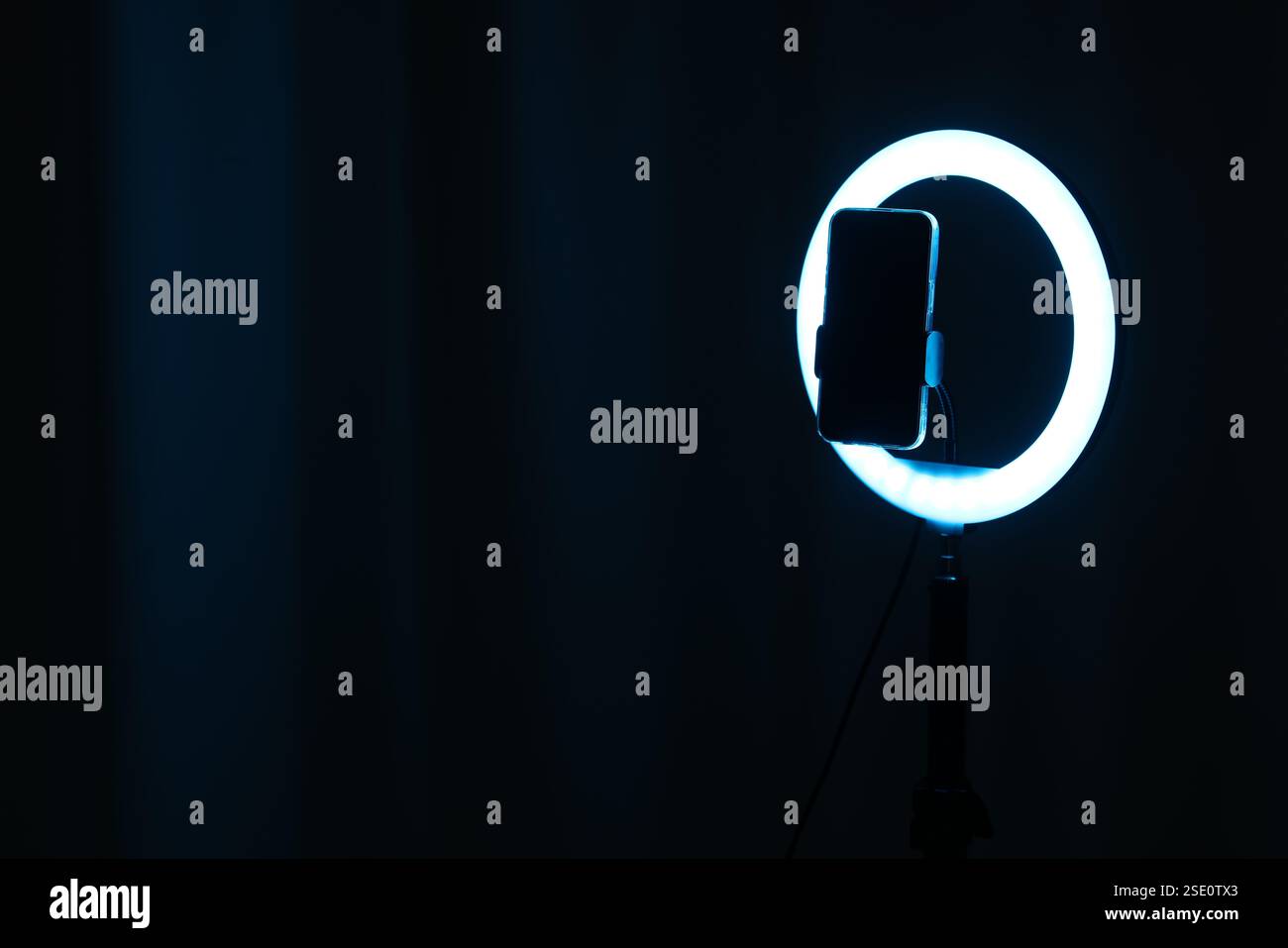 Glowing ring lamp with smartphone on black background. Space for text Stock Photo