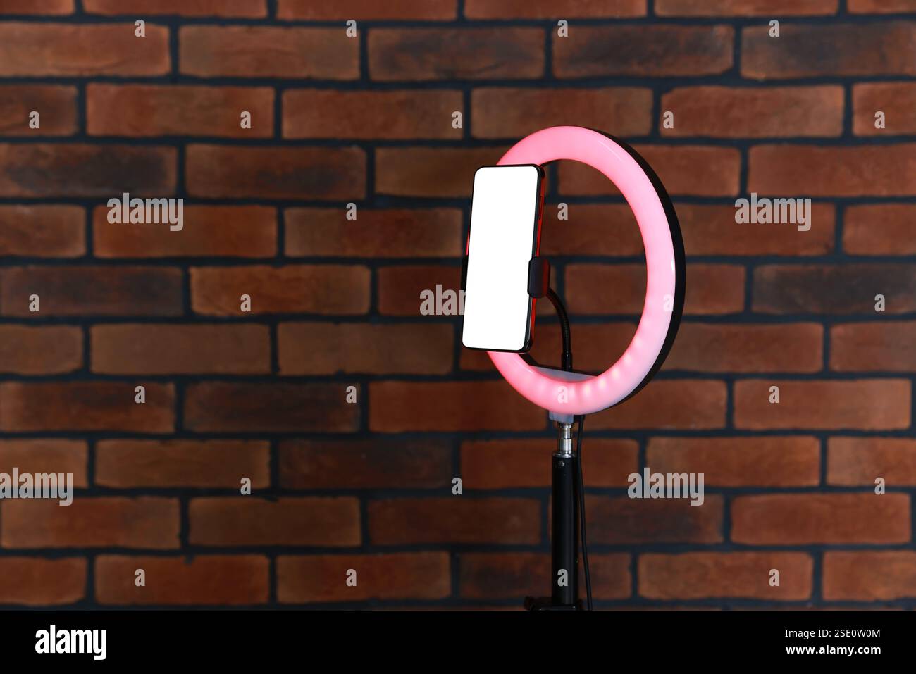 Ring lamp with smartphone against brick wall, space for text Stock Photo
