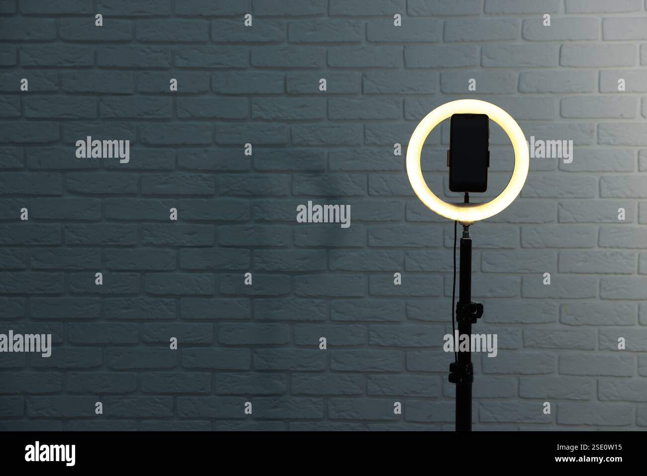 Ring lamp with smartphone against brick wall, space for text Stock Photo