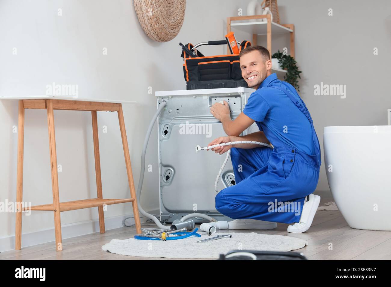 Male plumber repairing washing machine in bathroom Stock Photo