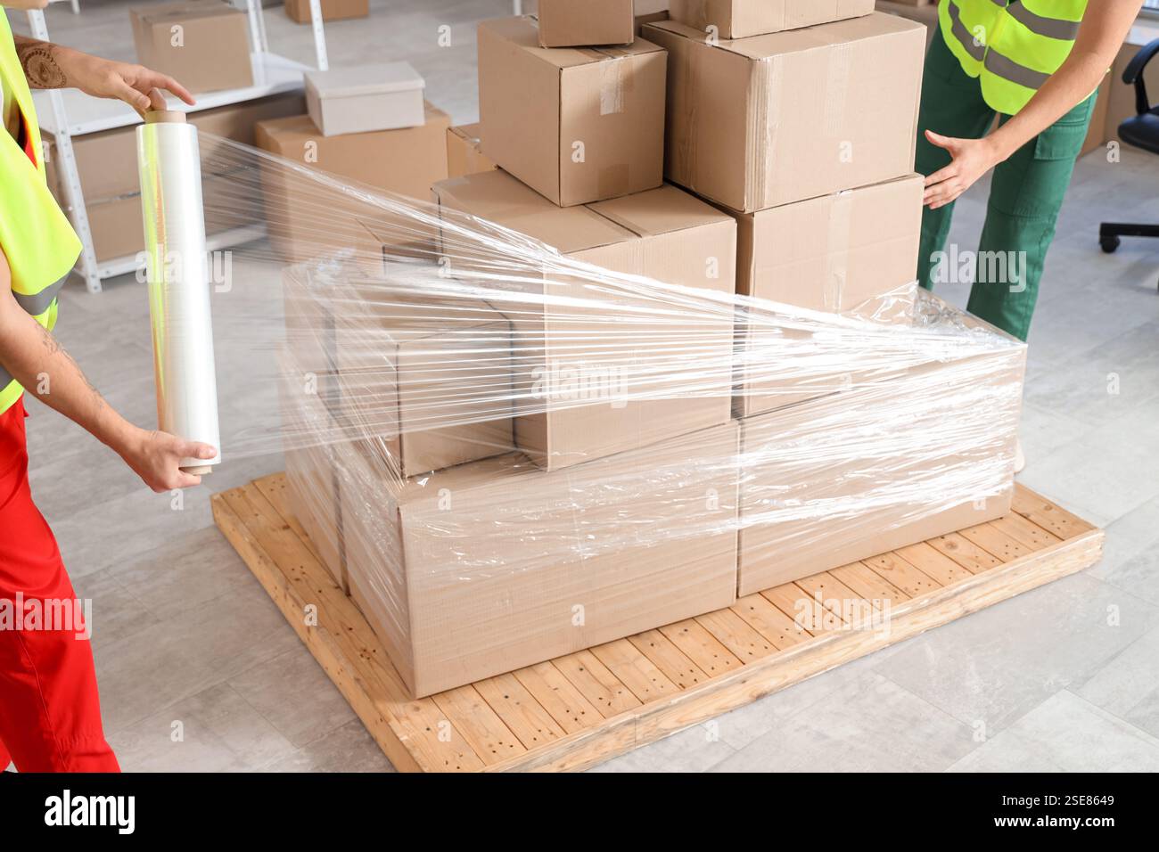 Male loaders wrapping boxes on pallet with stretch film in warehouse ...