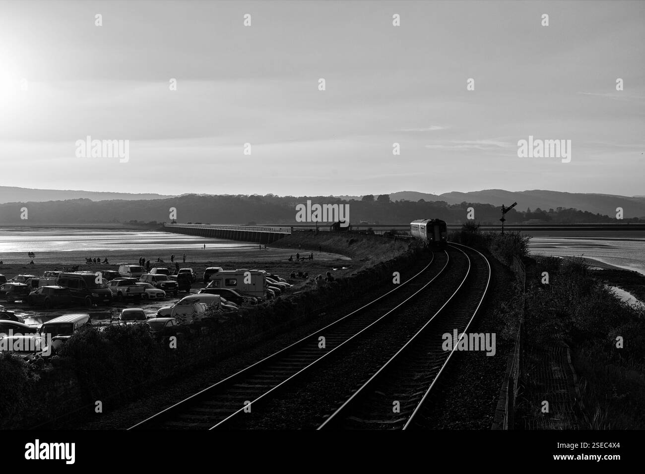 Northern rail class 156 super sprinter train Approaching Arnside viaduct on the scenic Cumbrian coast railway line glinting in the setting sun Stock Photo