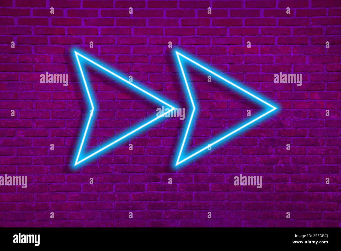 Bright neon arrow-shaped pointer on brick wall Stock Photo