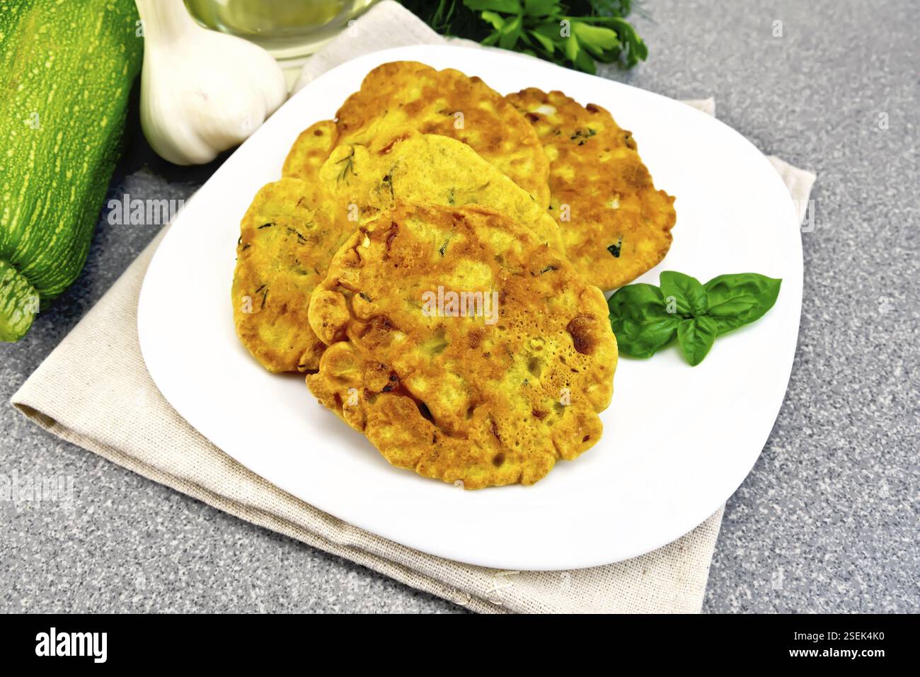 Indian chick-pea flour flatbreads with zucchini and fresh herbs, basil in a plate on a napkin, garlic and oil in the decanter on the background of the Stock Photo