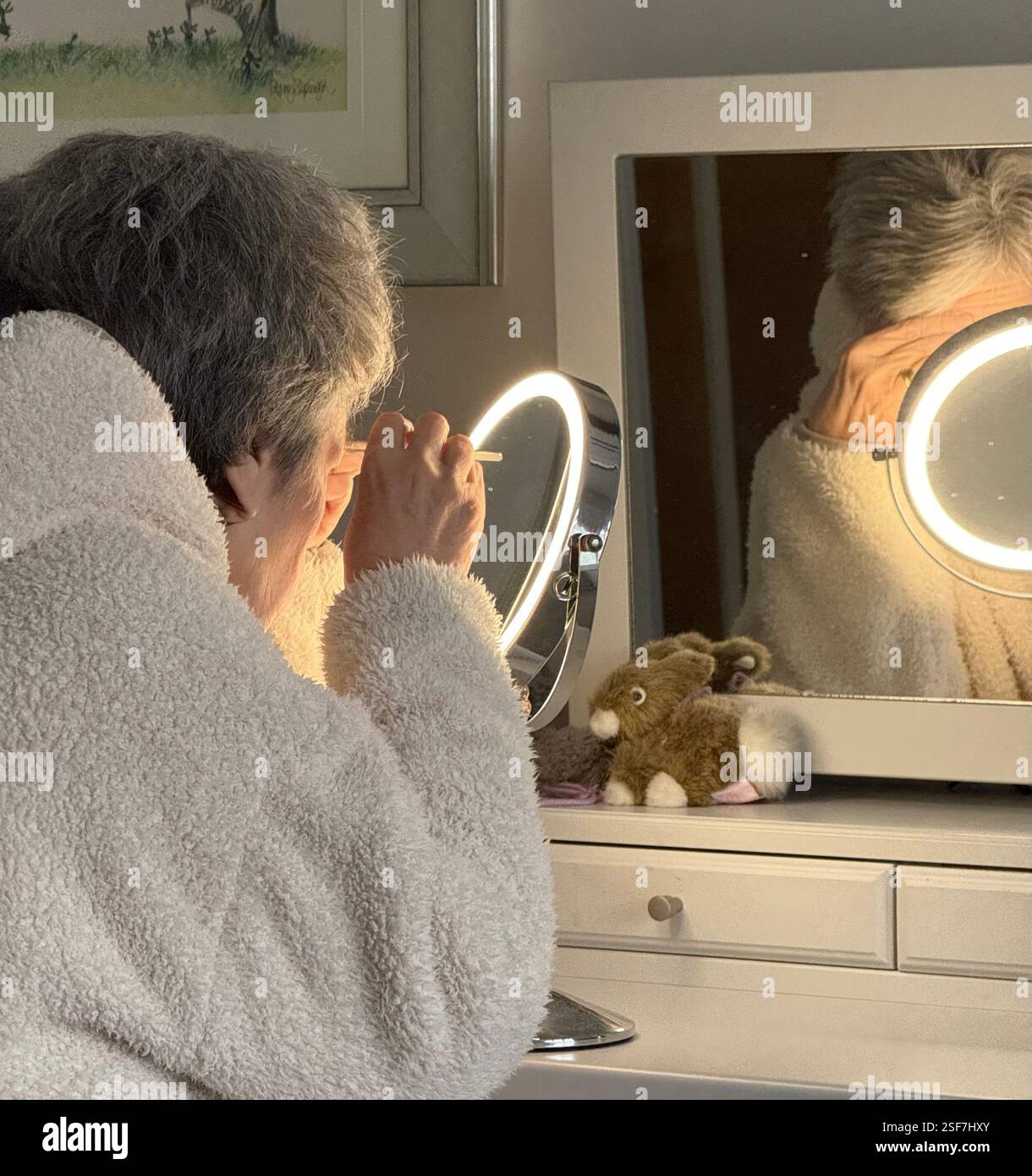 Lady in her dressing gown, at her bedroom dressing table using make up mirror - Smartphone Captured Stock Image