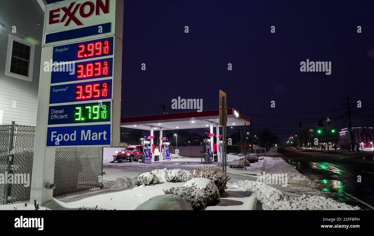 NORWALK, CT, USA - FEBRUARY 9, 2025: Exxon gas station encased in snow shows fuel prices as night falls on a quiet street in winter conditions. Stock Photo