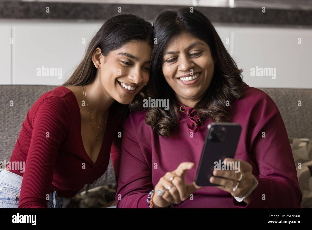 Smiling Indian woman and daughter using smartphone Stock Photo
