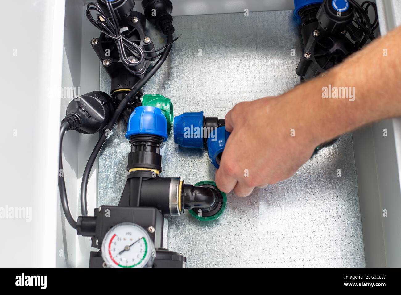 A man installs a drip irrigation system by placing a polypropylene compression tee into a metal box. Stock Photo