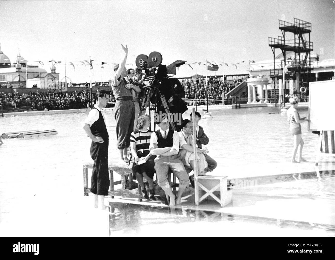 SING AS WE GO Director Basil Dean on location at the swimming baths in ...